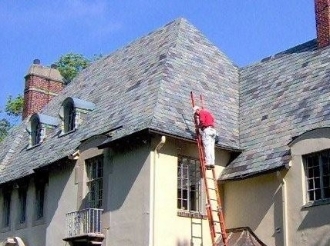 Person on ladder near steep house roof.